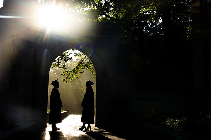 Silhouettes of a male and female graduate facing each other in an archway with sun rays in the background.